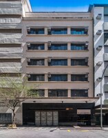 Um edifício de vários andares com fachada plana, aparelhos de ar condicionado e entrada no nível da rua identificada como 