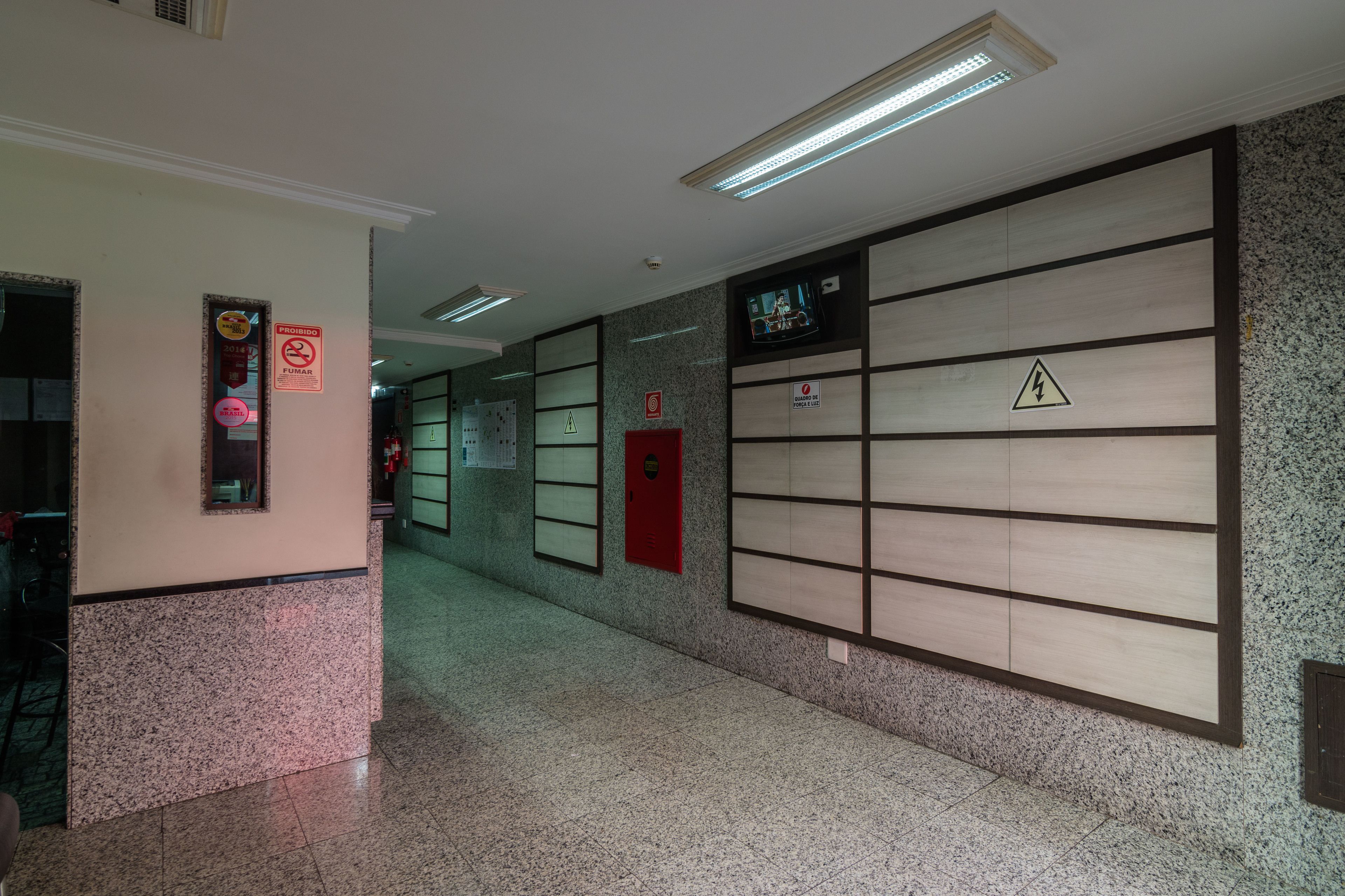 A hallway with a tiled floor, a red emergency phone, and a television screen mounted on the wall.