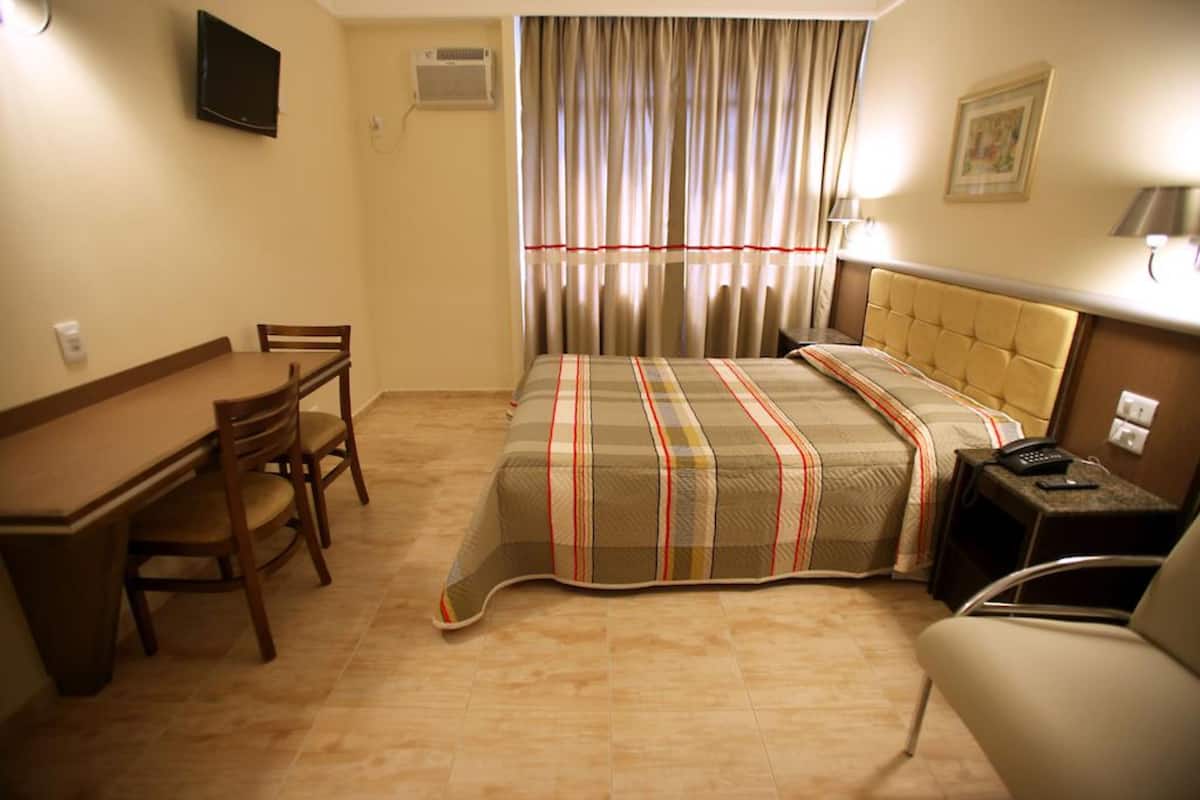 A hotel room with a bed, a desk, a chair, a TV, and a window with curtains.