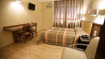 A hotel room with a bed, a desk, a chair, and a TV.