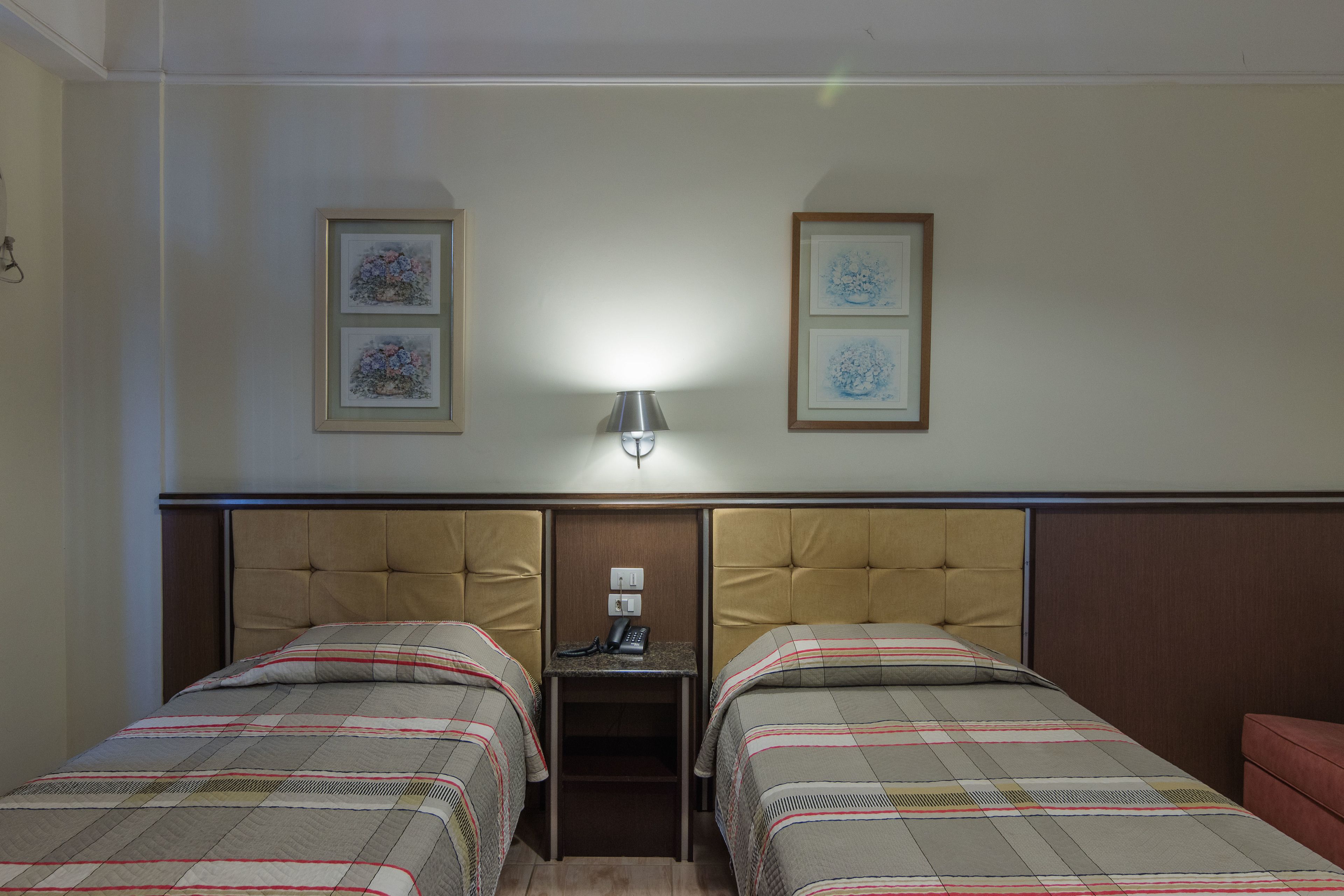 A hotel room with two beds, a nightstand with a lamp, and framed artwork on the wall.