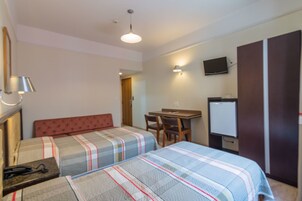 Quarto de hotel com duas camas, uma escrivaninha, uma cadeira, uma televisão e um guarda-roupa.