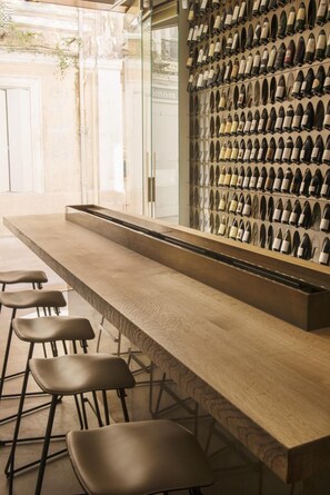 A bar area with a long counter and stools, a wall of wine bottles, and a glass partition.