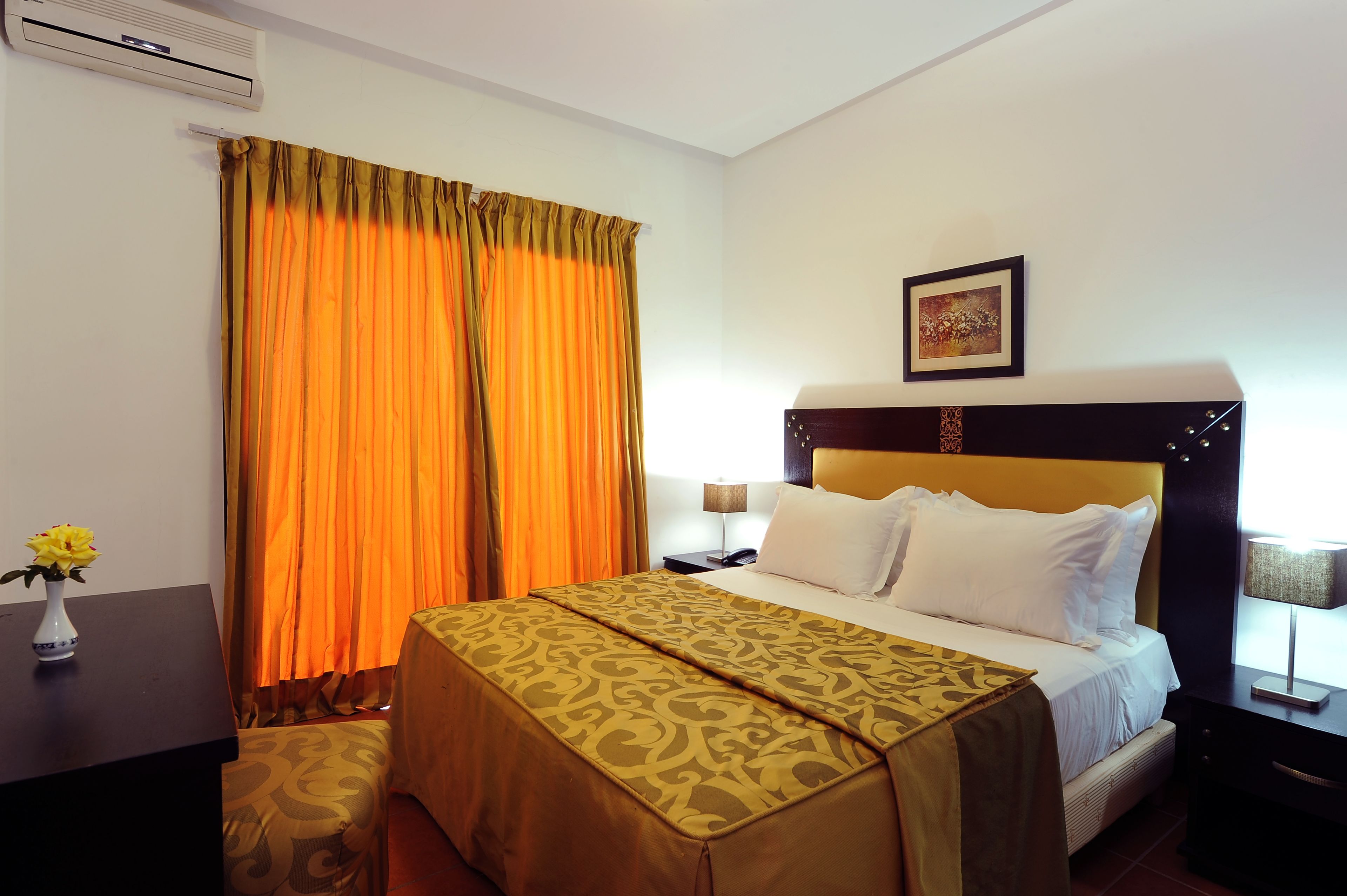 Une chambre d’hôtel avec un lit, une table de chevet avec une lampe, un climatiseur fixé au mur et un tableau encadré accroché au mur.