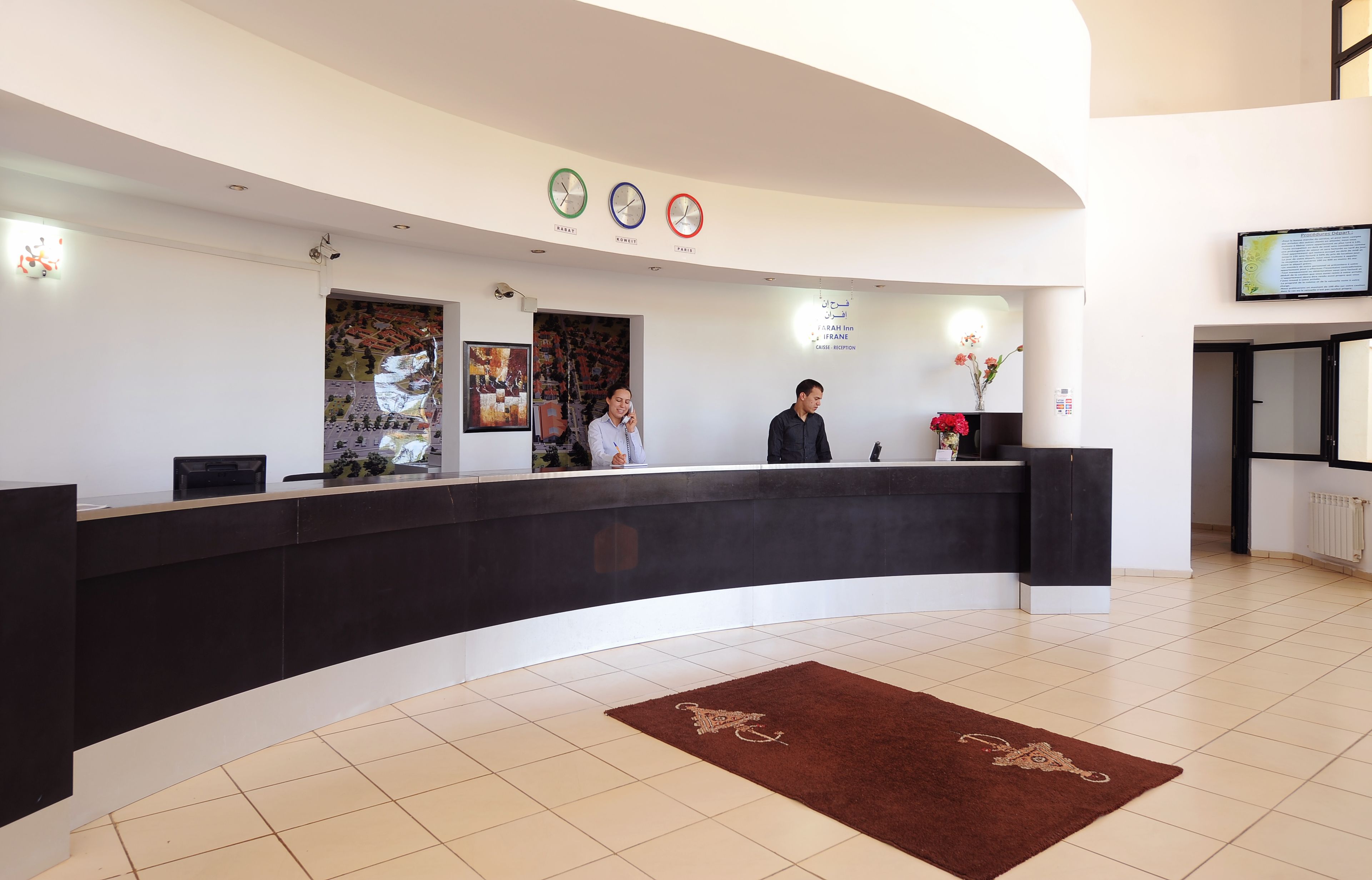 A reception area with a curved black counter, a brown rug, and a wall-mounted clock.