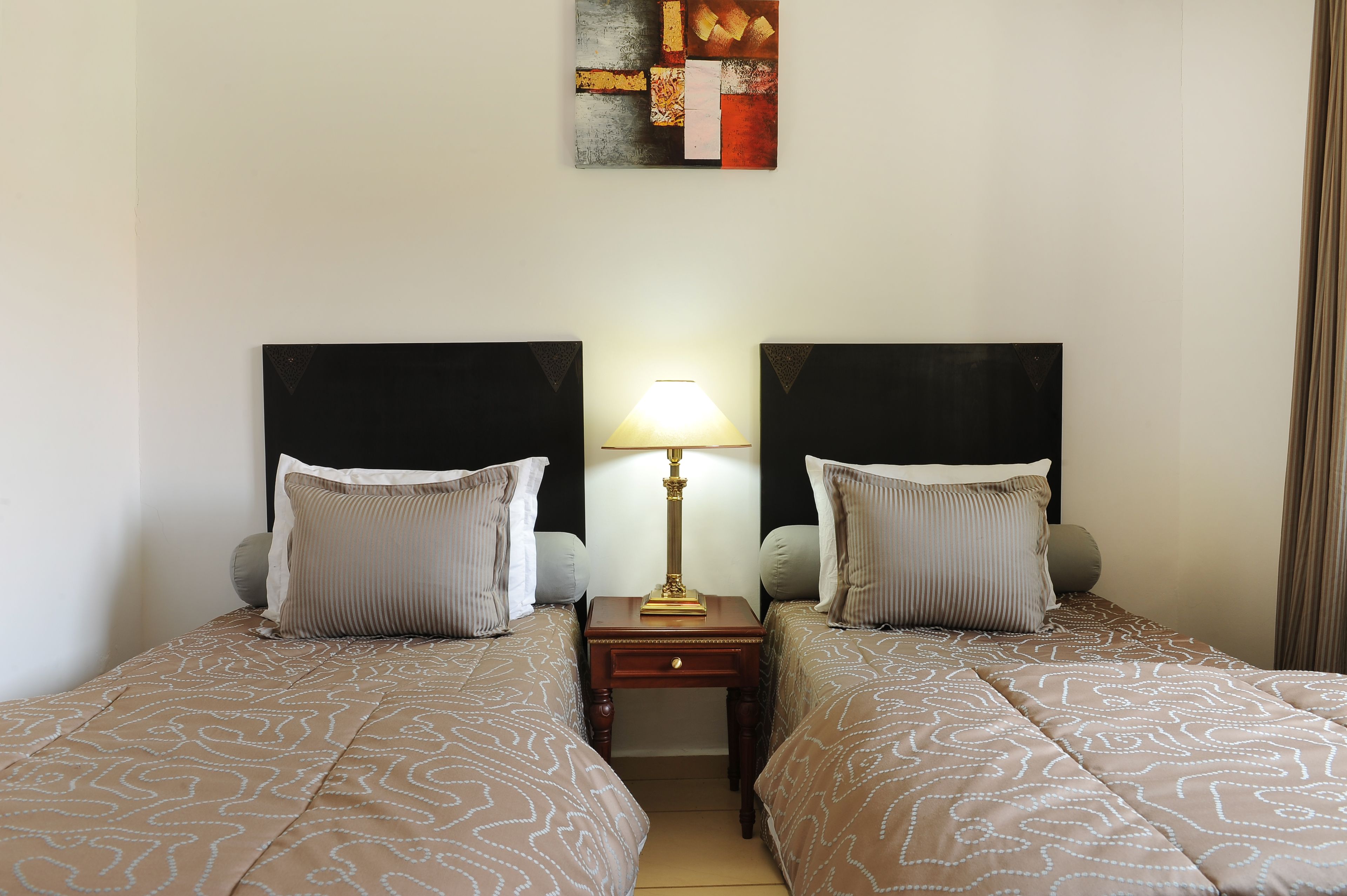 A hotel room with two beds, a nightstand with a lamp, and a painting on the wall.