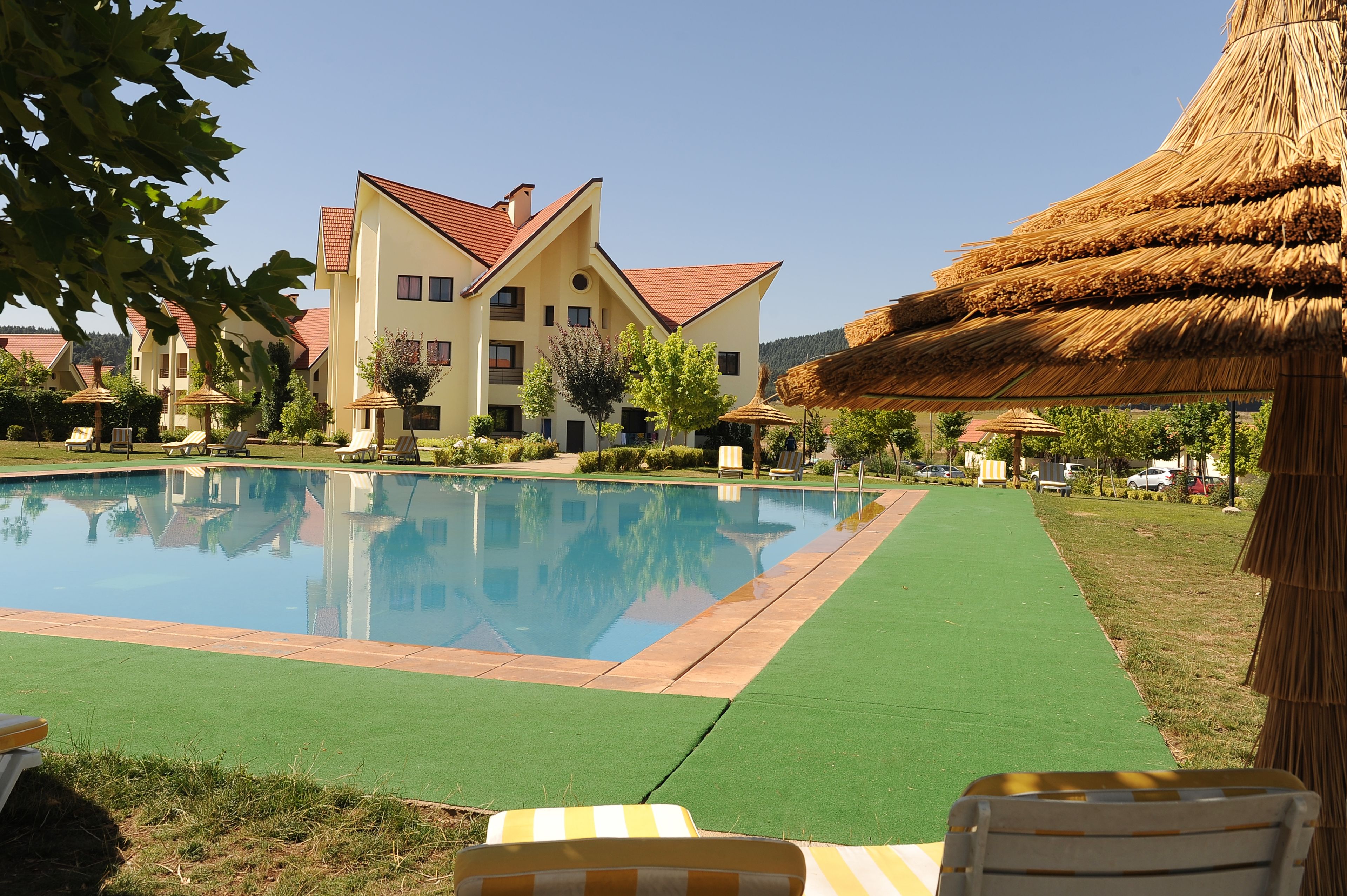 A swimming pool surrounded by lounge chairs and a large building with a red roof.
