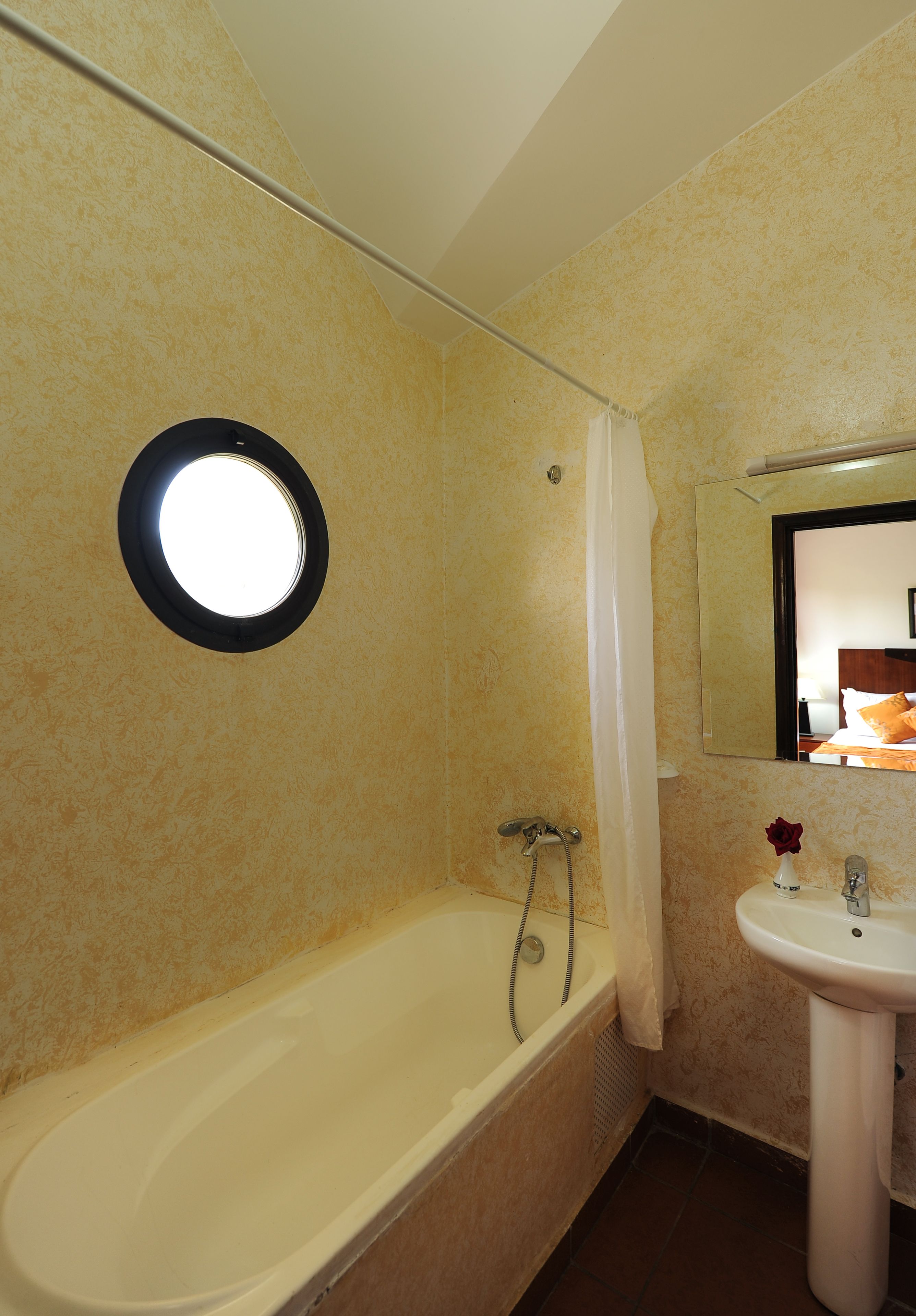 Un baño con bañera, lavamanos, espejo y un ventanal circular.
