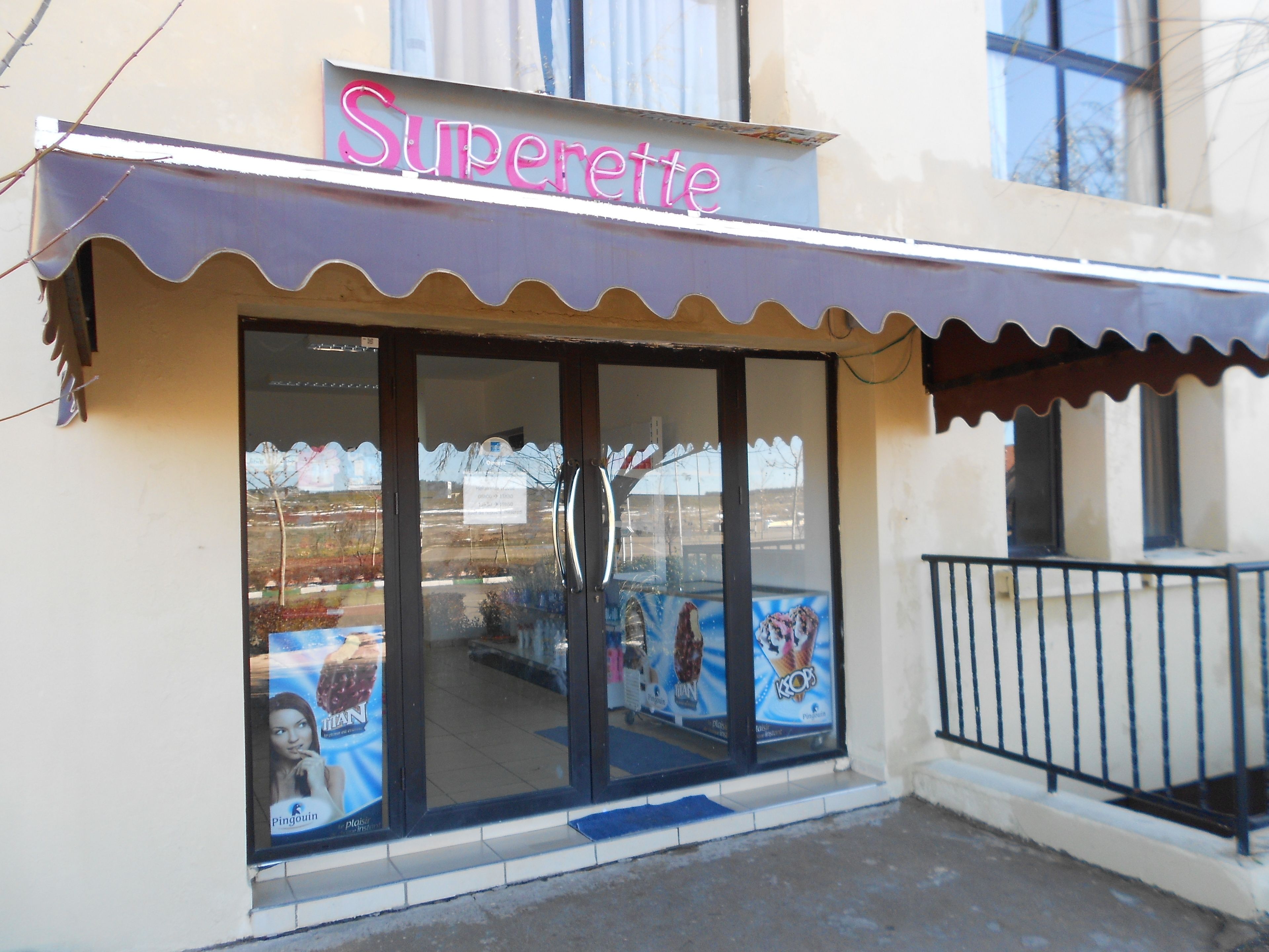 A storefront with a sign reading "Superette" and large glass windows displaying advertisements.