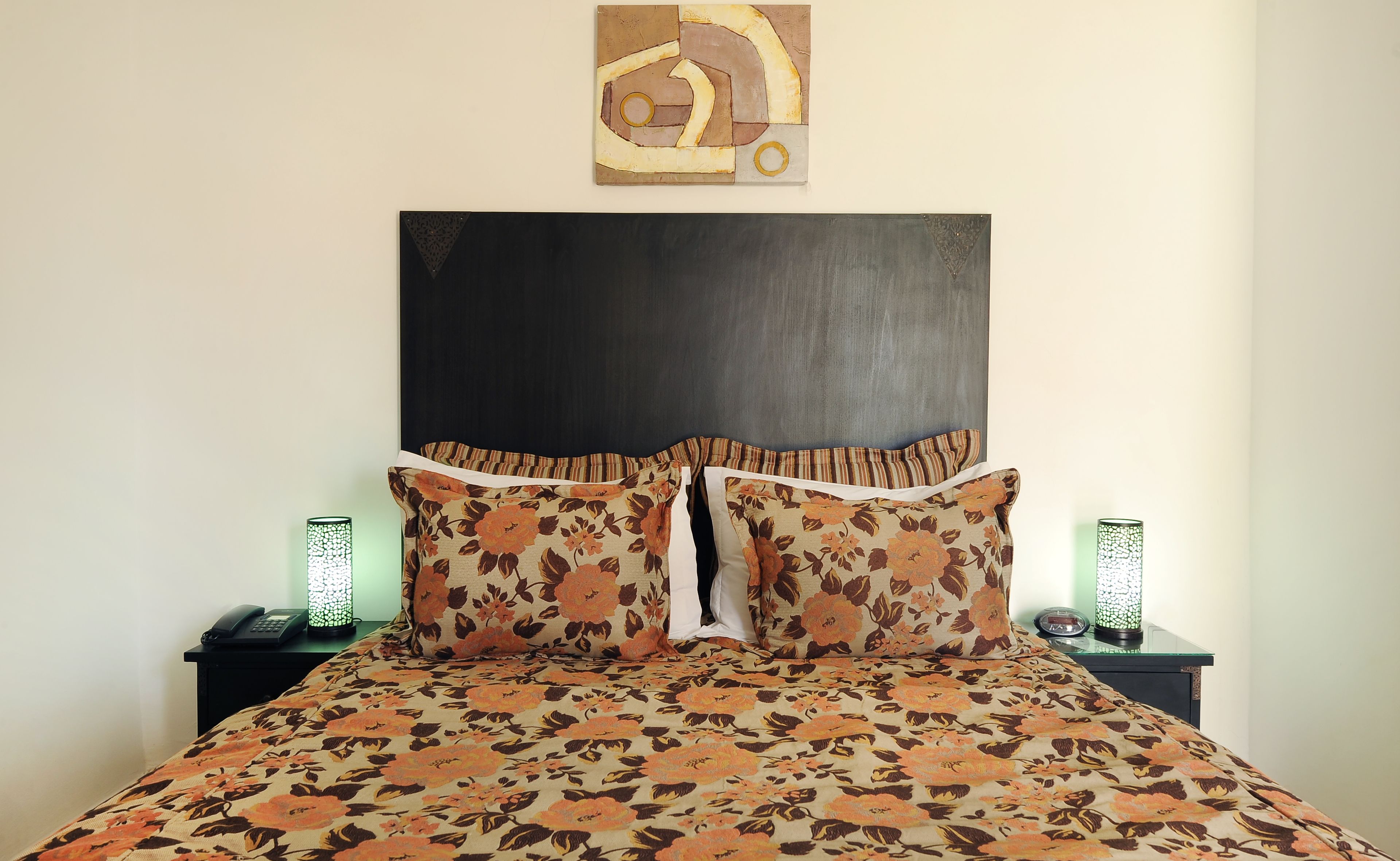 A bed with a floral bedspread, two pillows, a dark headboard, and two bedside tables with lamps.