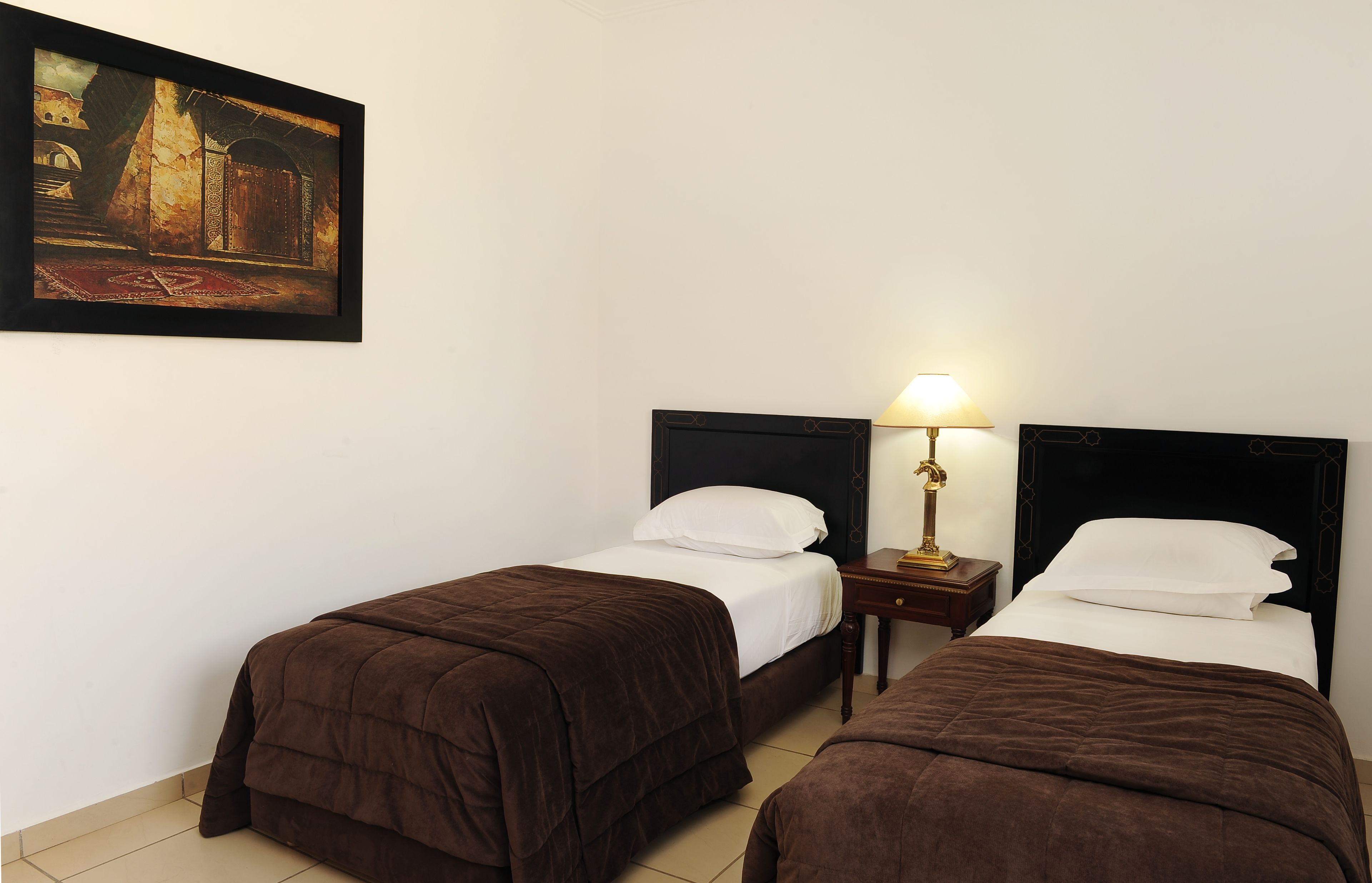 A hotel room with two beds, a nightstand with a lamp, and a painting on the wall.