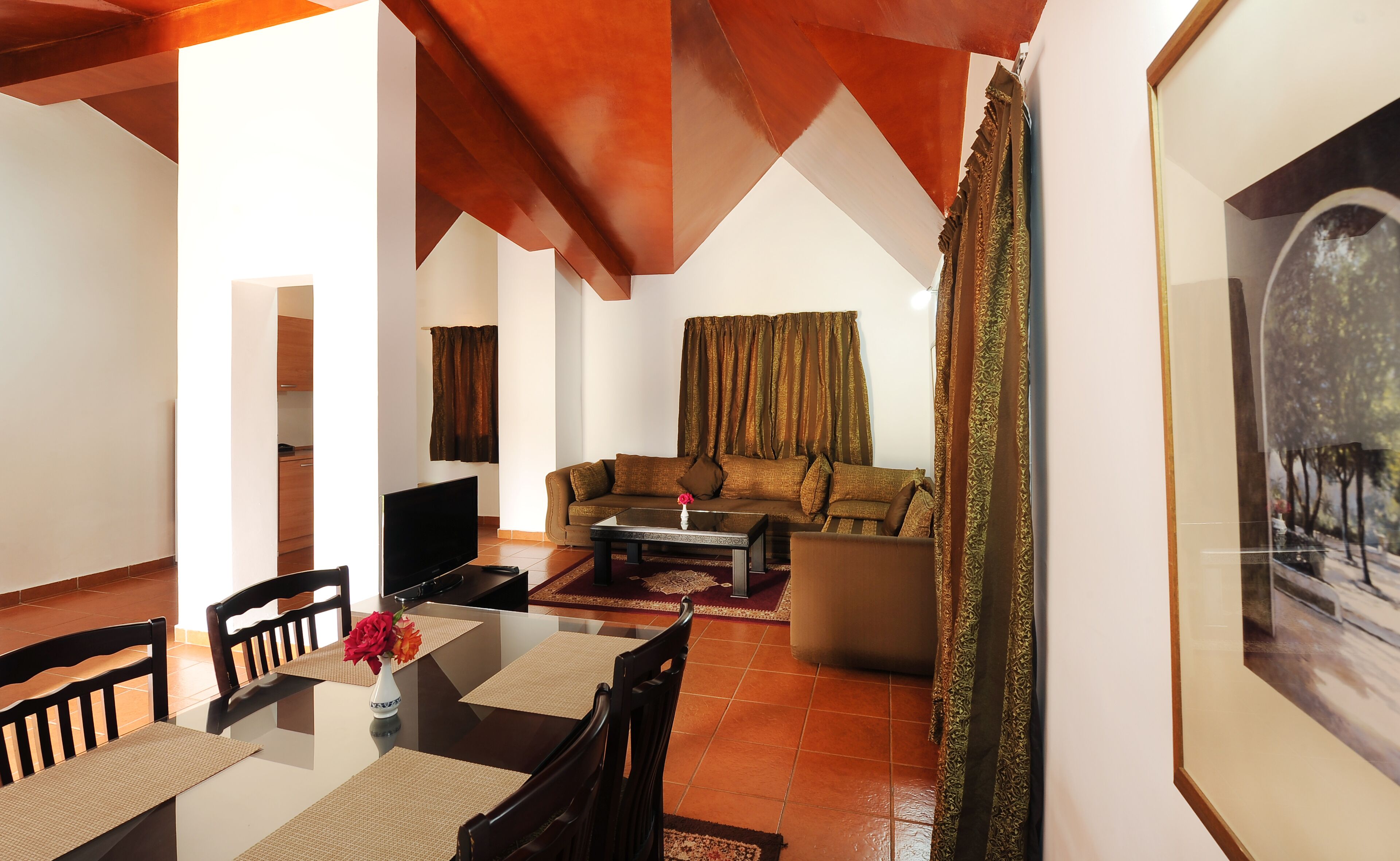 A living room with a sofa, coffee table, and chairs, a TV, and a painting on the wall.