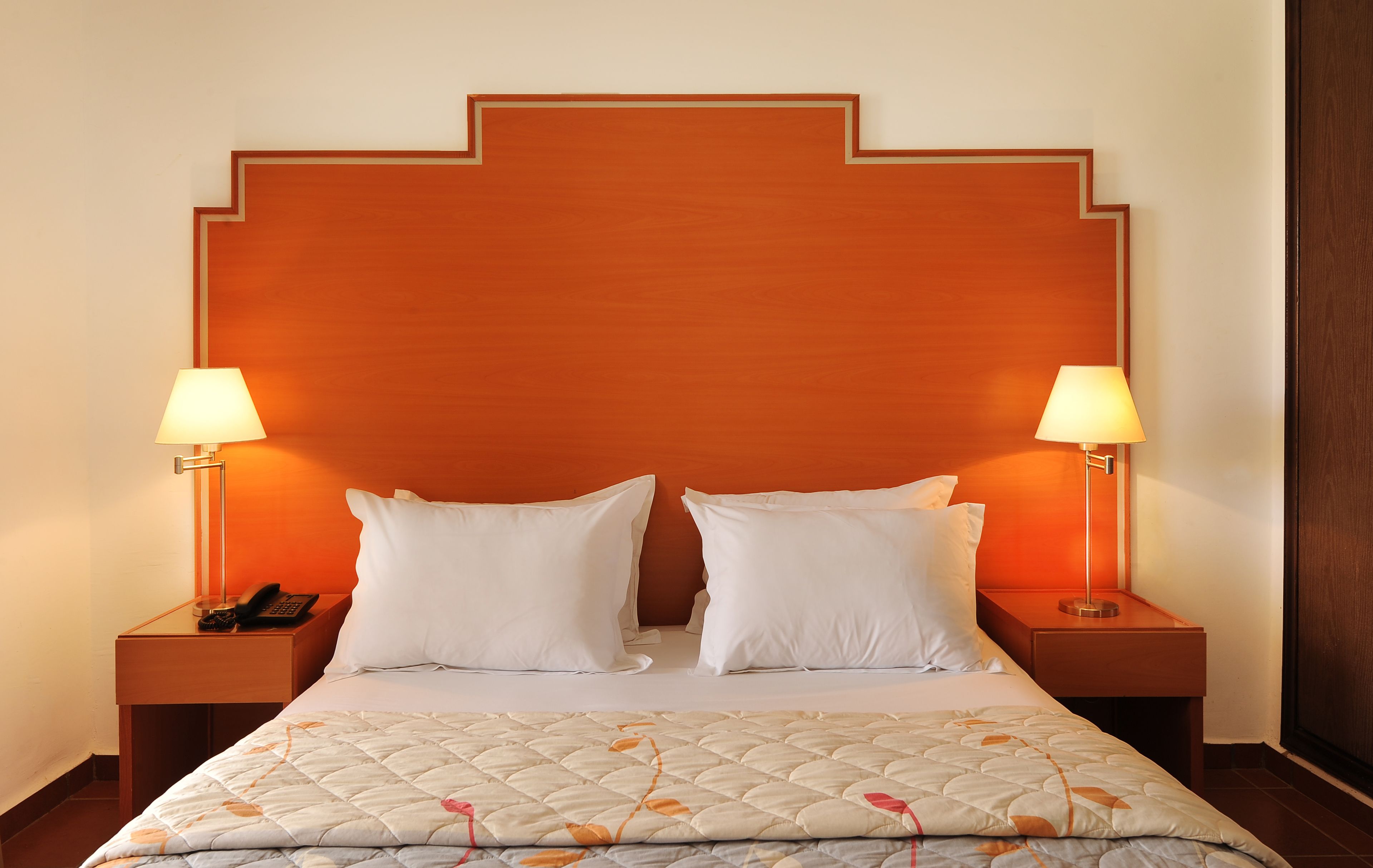 Een hotelkamer met een groot bed, twee bedlampen, een telefoon en een houten hoofdeinde.
