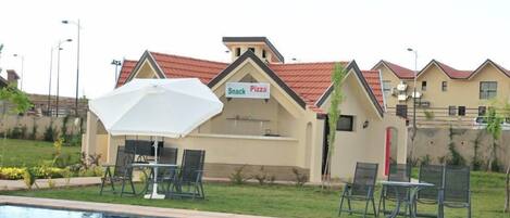 A poolside area with a 'Snack Pizza' sign, outdoor seating, and a pool.