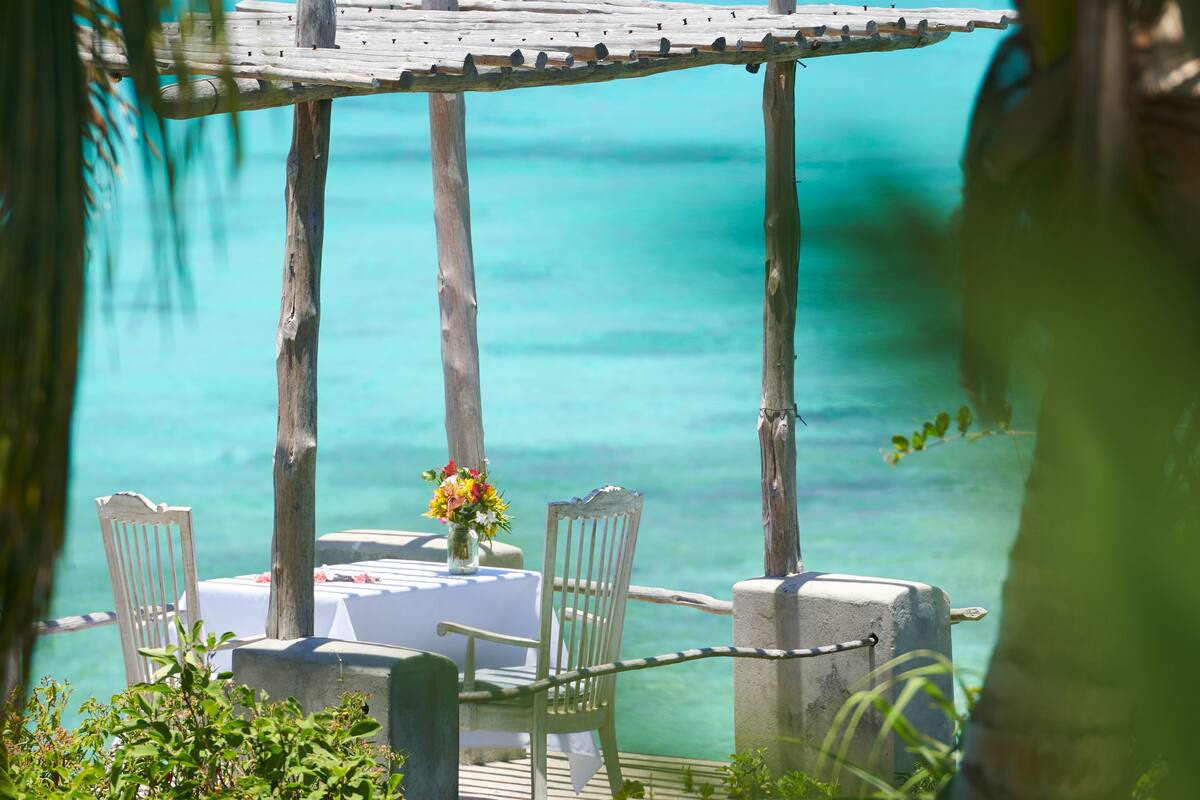 A wooden pergola with a table and chairs overlooking a turquoise sea.