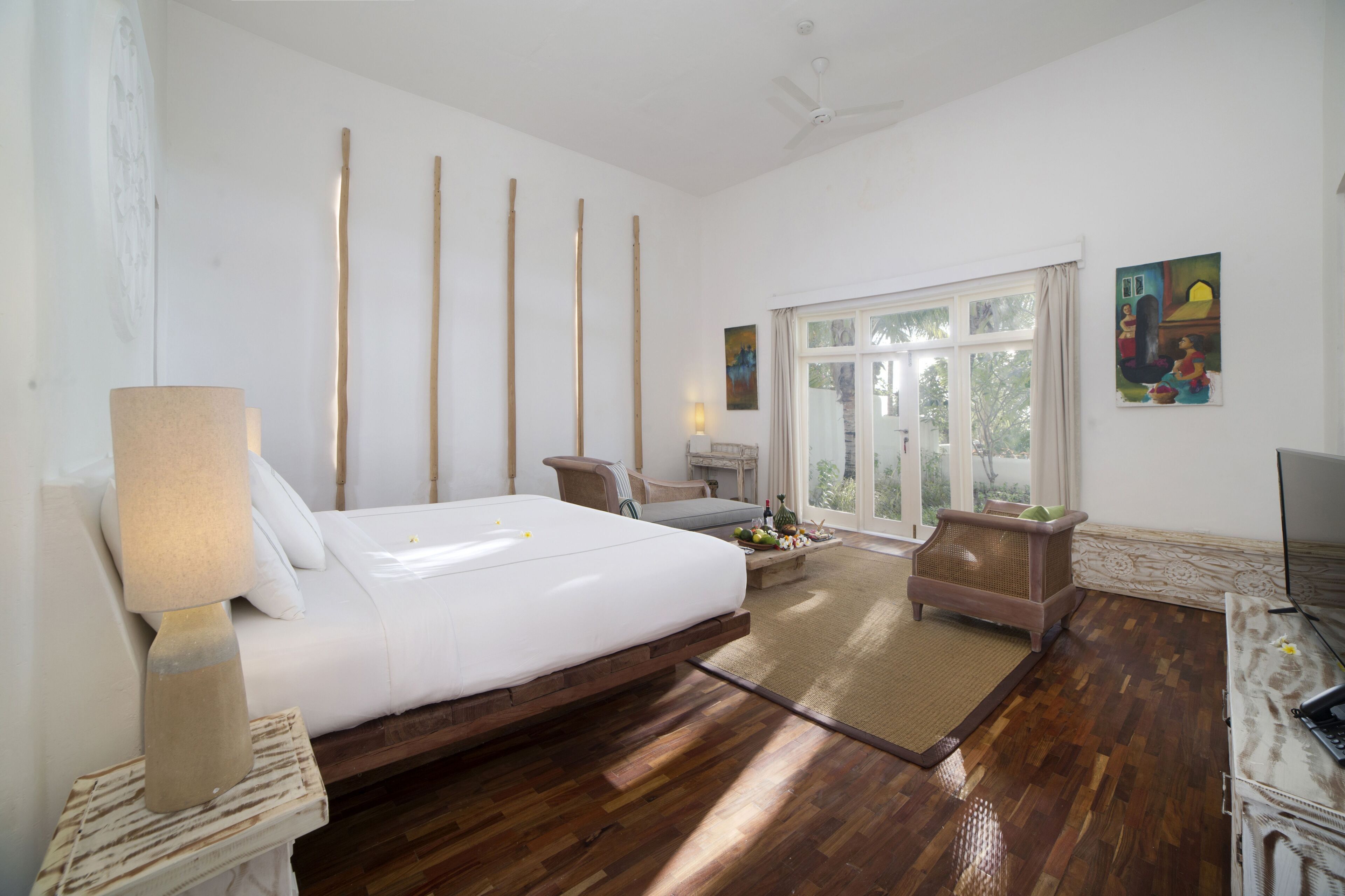 A bedroom with a bed, bedside table, lamp, and a view of the outdoors through a large window.
