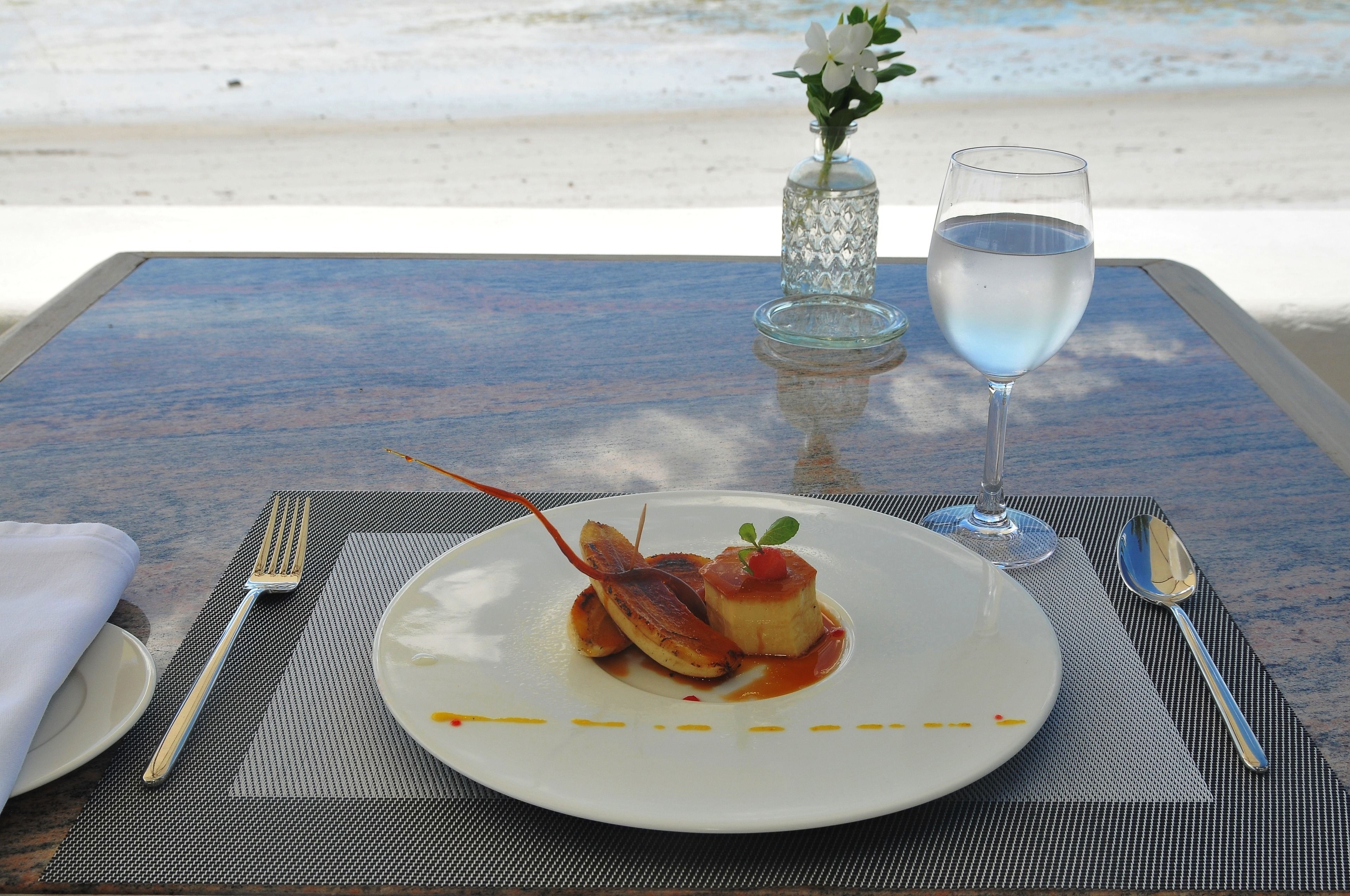 A table set with a plate of food, a glass of water, and a vase with flowers.