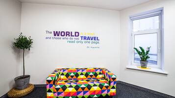 A room with a colorful geometric-patterned sofa, a potted plant, and a wall quote about travel.