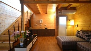 A cozy cabin interior with a wooden staircase, a kitchenette, a sofa, and a small dining table. - Orabella Villas & Suites (Calangute)