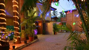 A courtyard with potted plants and palm trees, surrounded by wooden buildings with a brick pathway. - Orabella Villas & Suites (Calangute)