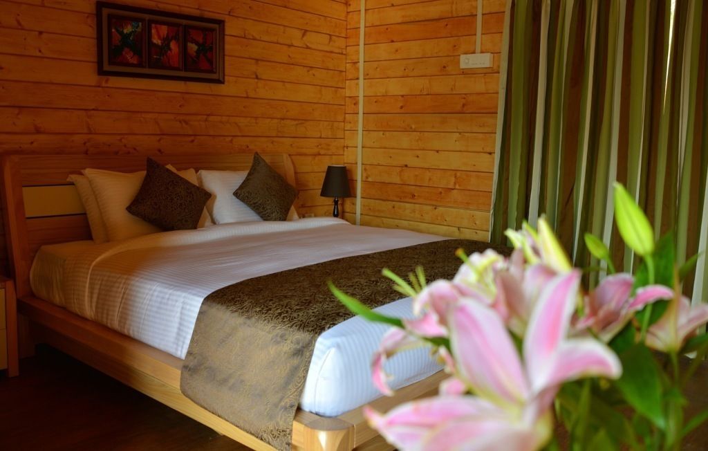 A wooden-paneled room with a bed, pillows, a nightstand, a lamp, and a framed picture on the wall.