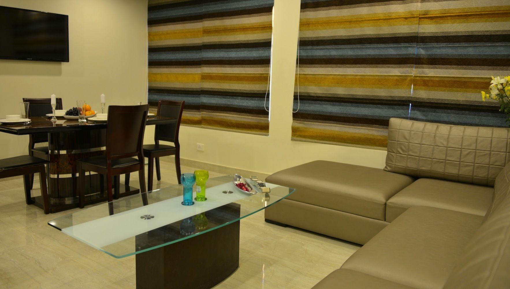 Un salon moderne avec une table basse en verre, un canapé beige et un mur à rayures.
