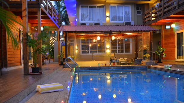 A poolside area with a wooden deck, a pool, and a covered seating area with tables and chairs. - Orabella Villas & Suites (Calangute)