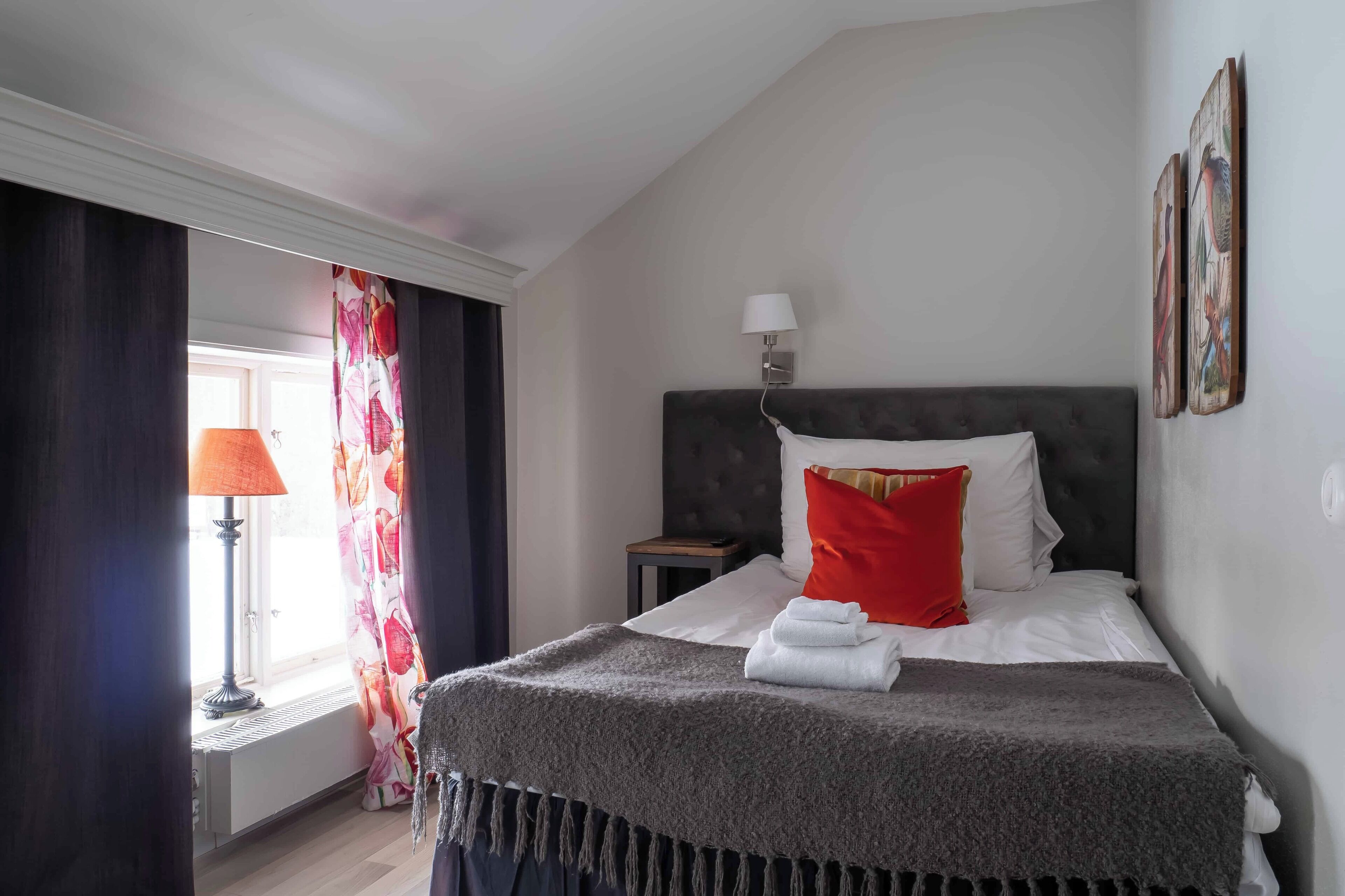 Una habitación de hotel con una cama, una mesita de noche, una lámpara y una ventana con cortinas.