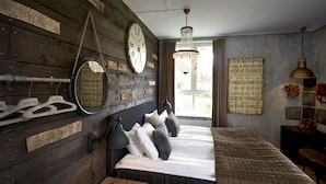 Un dormitorio rústico con pared de madera, una cama con muchos cojines, una lámpara colgante y un reloj de pared grande.
