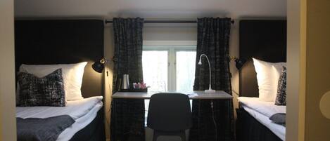 Una habitación tipo dormitorio con dos camas individuales, un escritorio, una silla y una ventana con cortinas.
