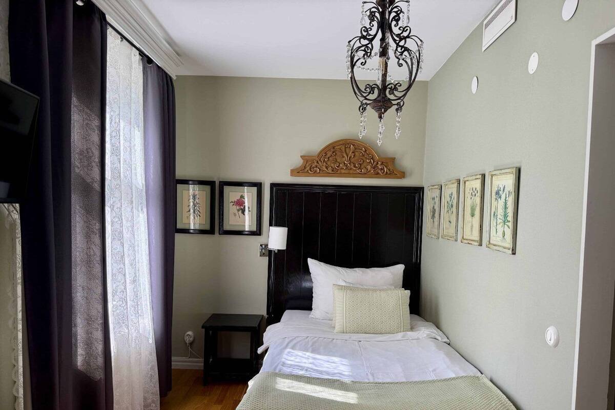 Un dormitorio con cama, mesita de noche, candelabro e impresiones botánicas enmarcadas en la pared.