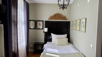 A bedroom with a bed, a nightstand, a chandelier, and framed botanical prints on the wall.