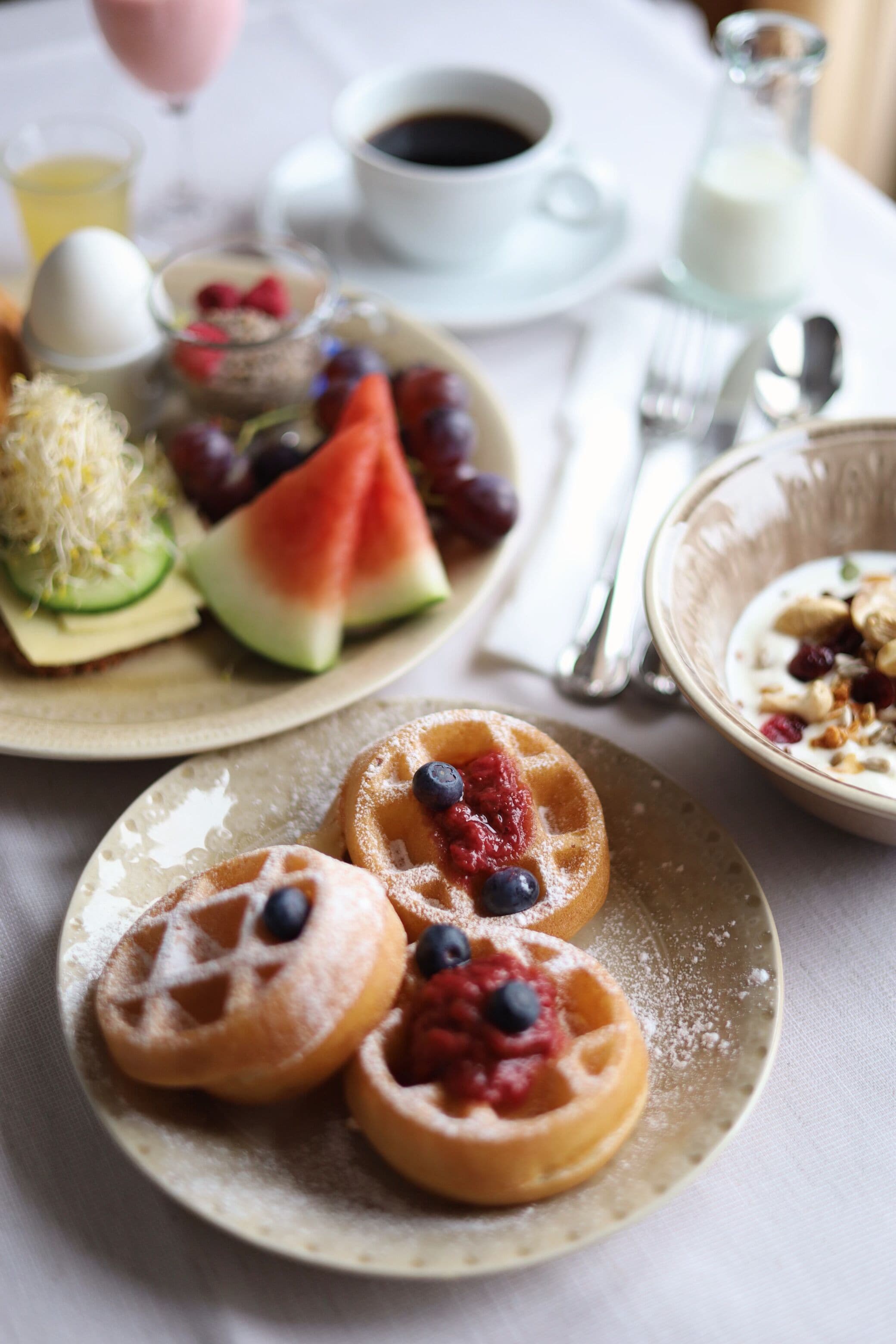 A breakfast setting with waffles topped with berries, a glass of orange juice, and a cup of coffee on a table.