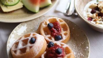 A breakfast setting with waffles topped with berries, a glass of orange juice, and a cup of coffee on a table.