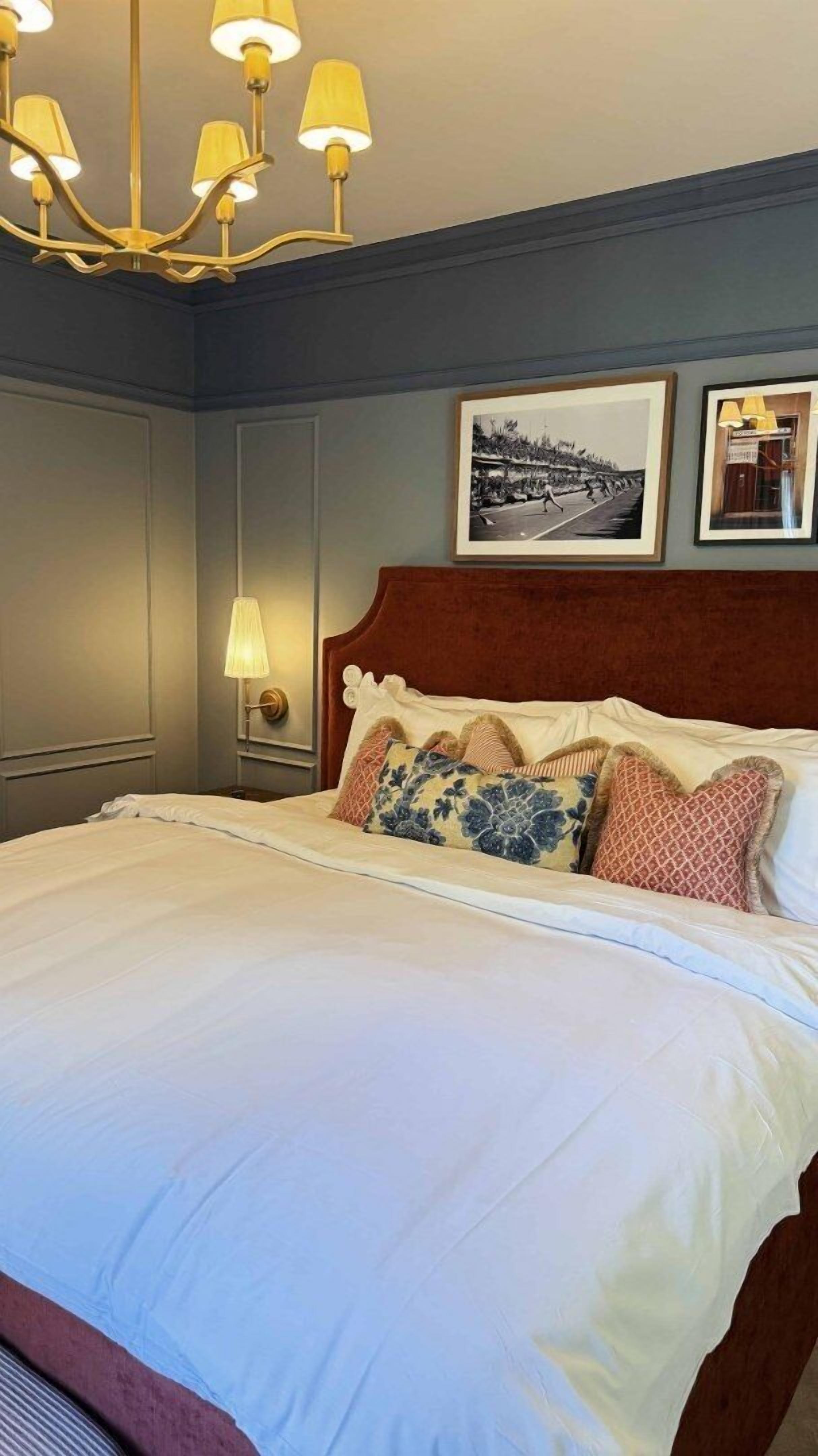 Una habitación de hotel con una cama grande, una araña, un cuadro en la pared y una mesita de noche con una lámpara.