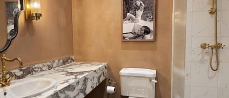 Un baño con lavamanos de mármol, inodoro, ducha y un cuadro en la pared.