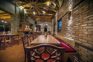 A restaurant with a long wooden table, red cushioned benches, and exposed brick walls. - Montanema Handmade Village (Mouzaki)