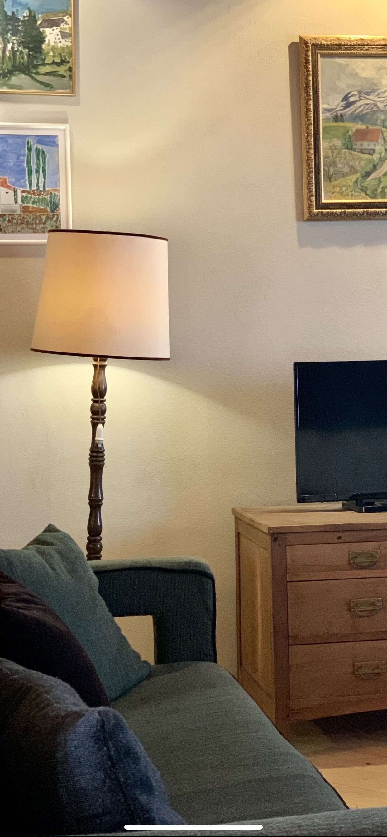 A room with a green sofa, a wooden cabinet with drawers, a television on top, and a lamp with a beige shade.