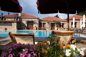 A poolside area with stone buildings, outdoor seating, and umbrellas. - Montanema Handmade Village (Mouzaki)