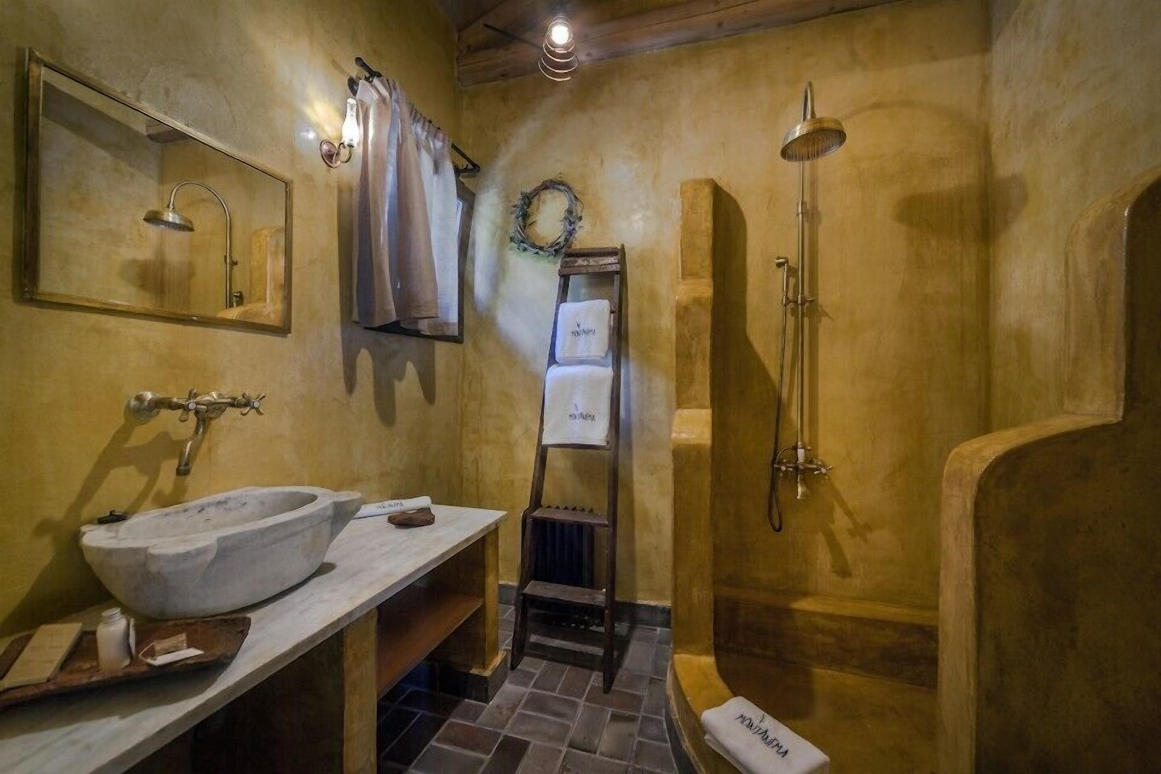 Een rustieke badkamer met een stenen wasbak, een houten trapje, een douche en een handdoekhouder.
