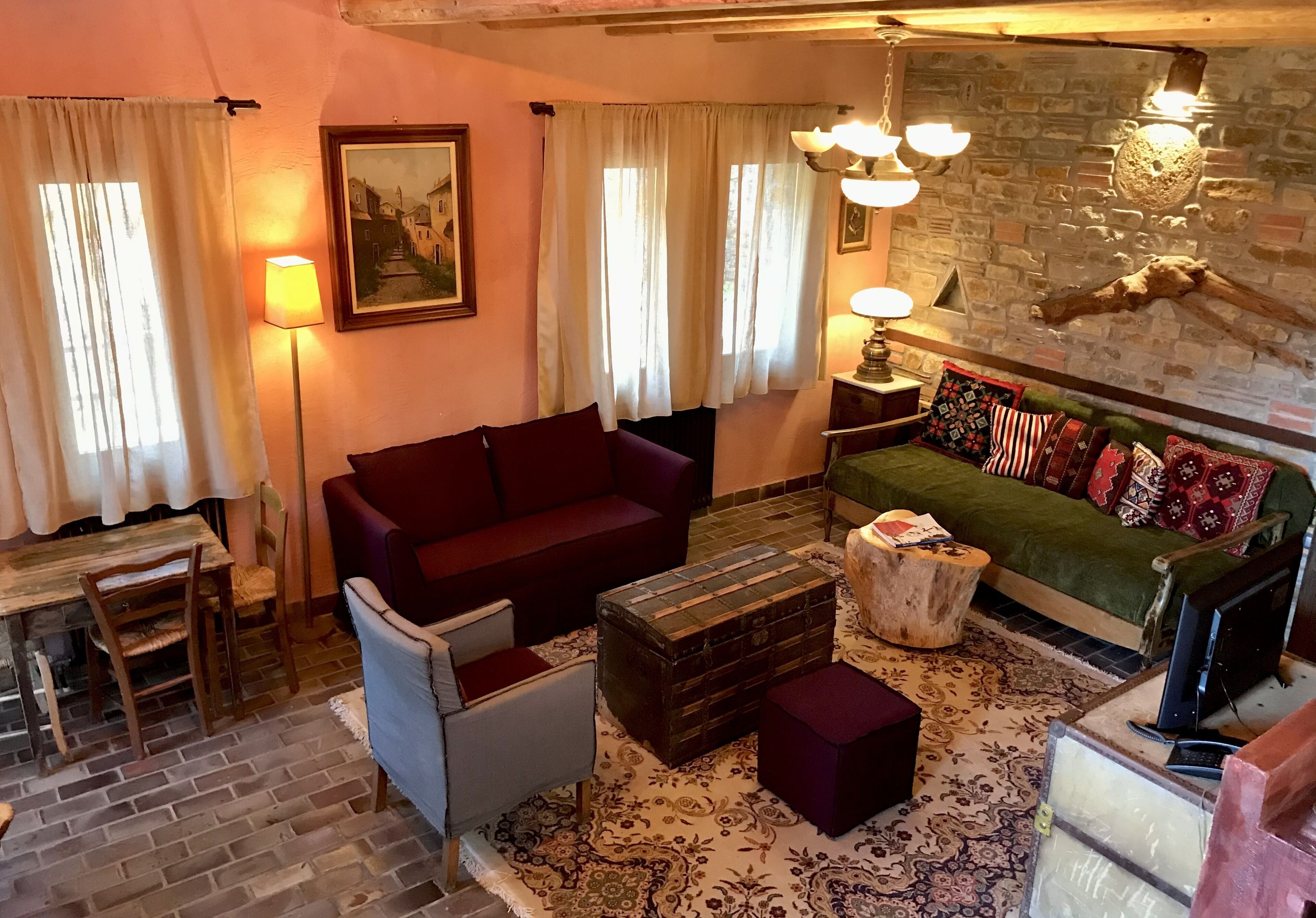 A cozy living room with a red sofa, a green sofa with patterned cushions, a wooden coffee table, and a rustic brick wall.