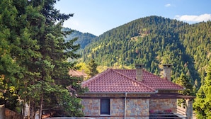 A stone building with a red-tiled roof, wooden railings, and a gravel path leading to it. - Montanema Handmade Village (Mouzaki)