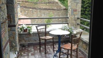 Un patio con paredes de piedra, una mesa redonda y dos sillas, un farol, y vista a una zona boscosa.