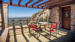 A terrace with a stone wall, wooden beams, and a table with chairs. - Montanema Handmade Village (Mouzaki)
