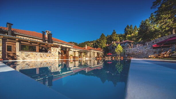 A stone building with a pool reflecting the structure. - Montanema Handmade Village (Mouzaki)
