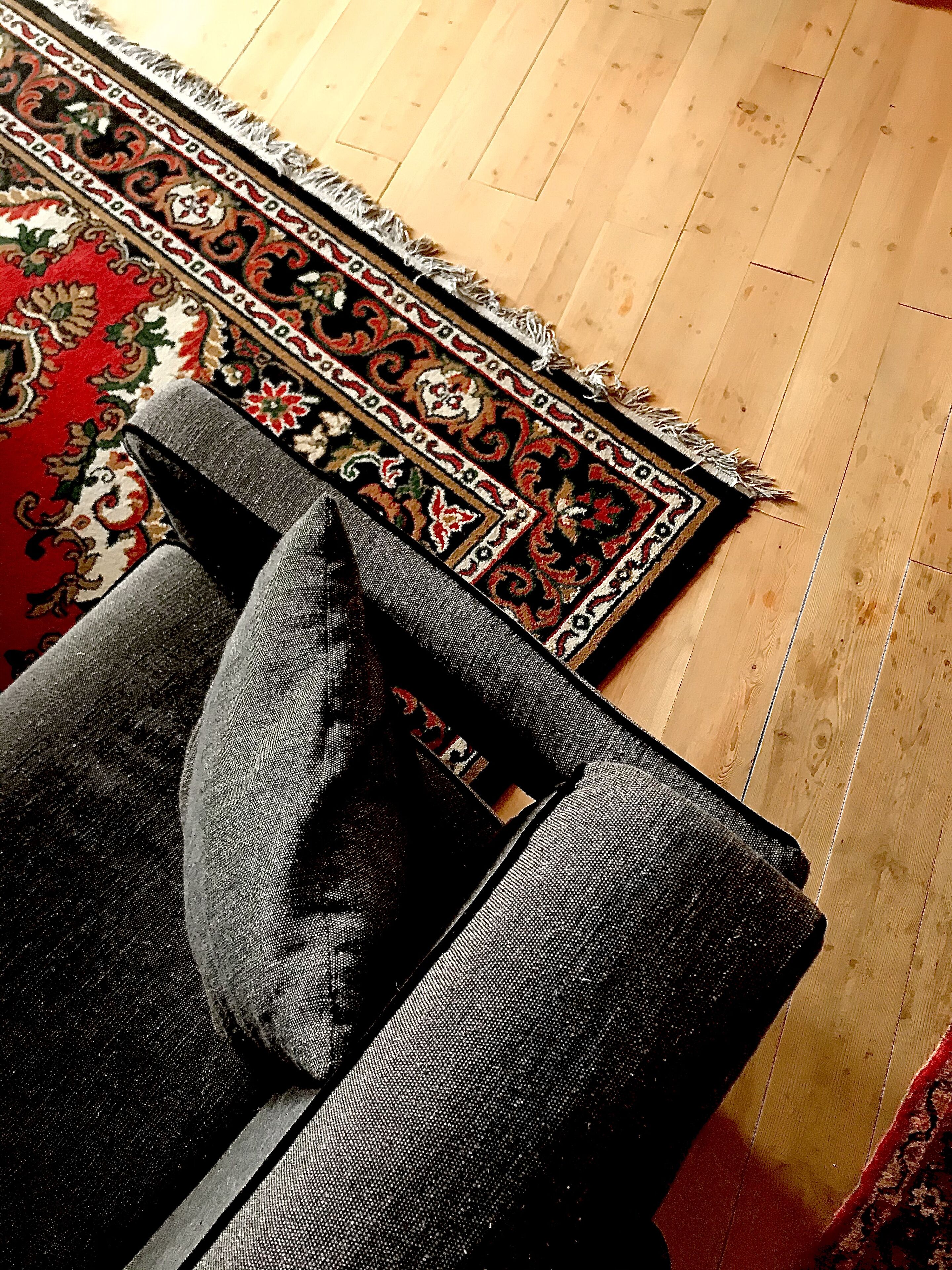 A wooden floor with a patterned rug and a grey upholstered chair.
