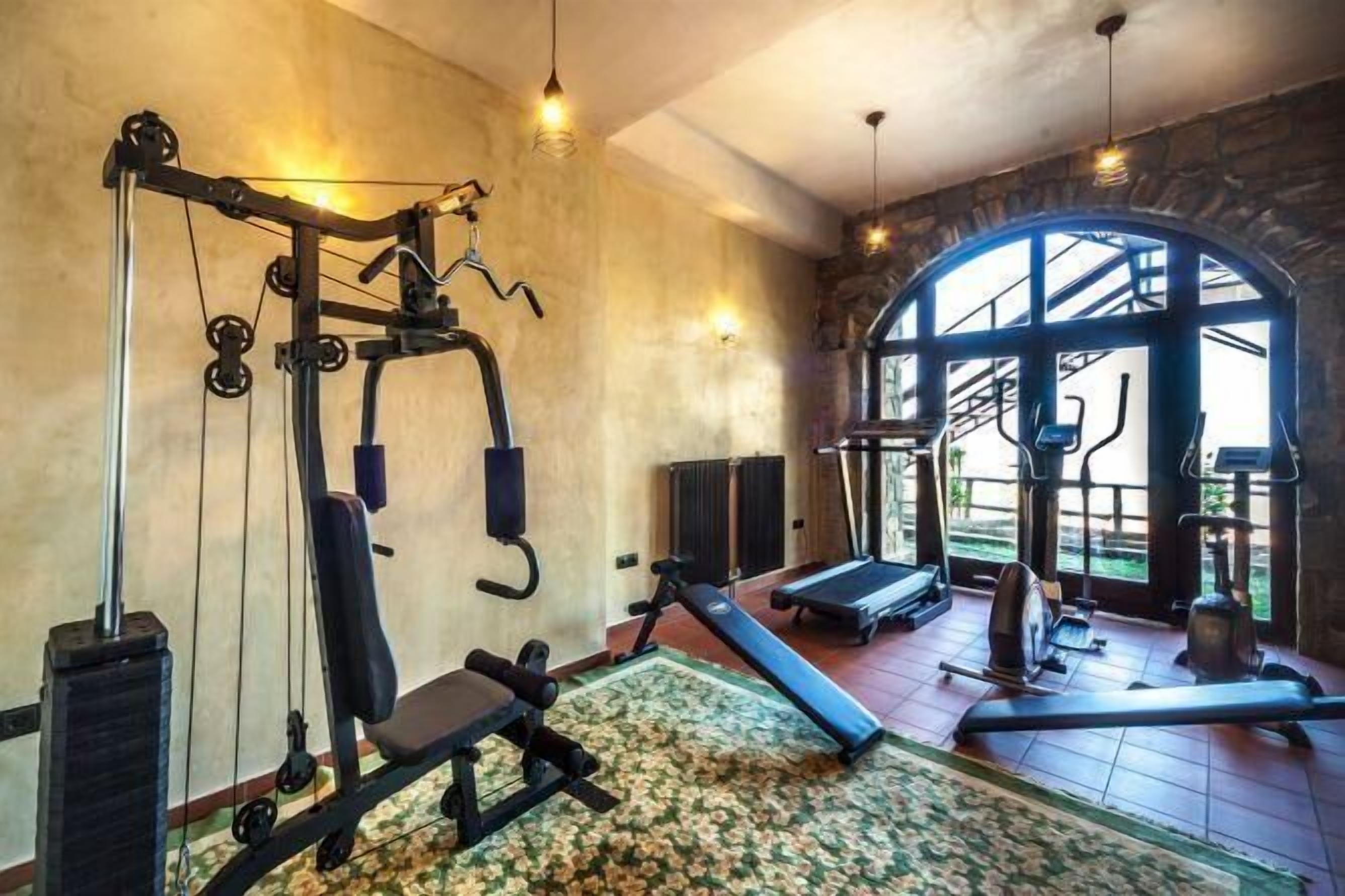 A gym with various exercise equipment, a large window, and a stone wall.