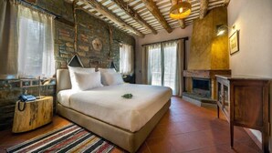 A spacious bedroom with a large bed, a stone wall, a fireplace, and a wooden ceiling. - Montanema Handmade Village (Mouzaki)