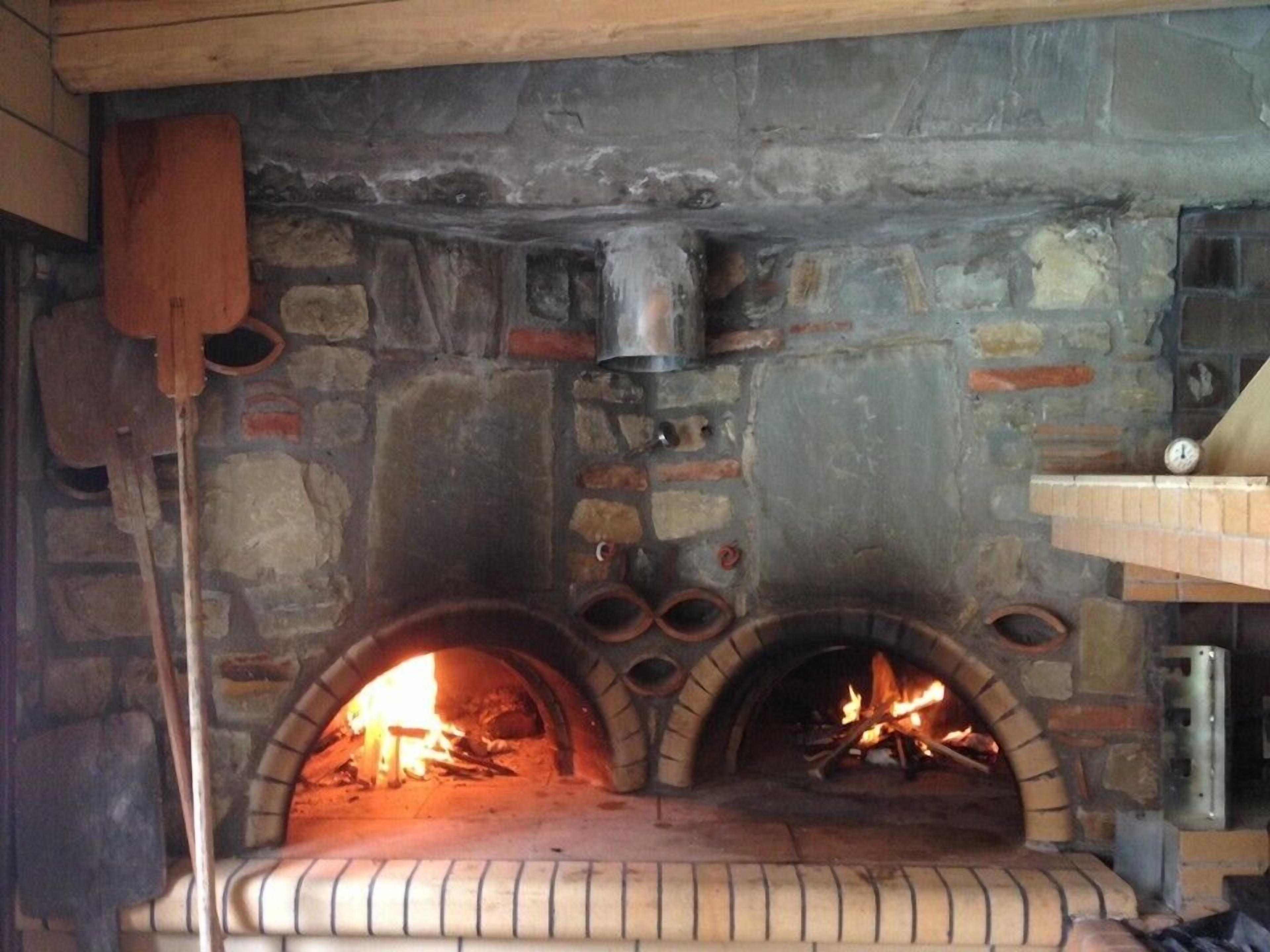 Una chimenea de piedra con dos fuegos, un estante de madera encima y una olla de metal colgada en la pared.