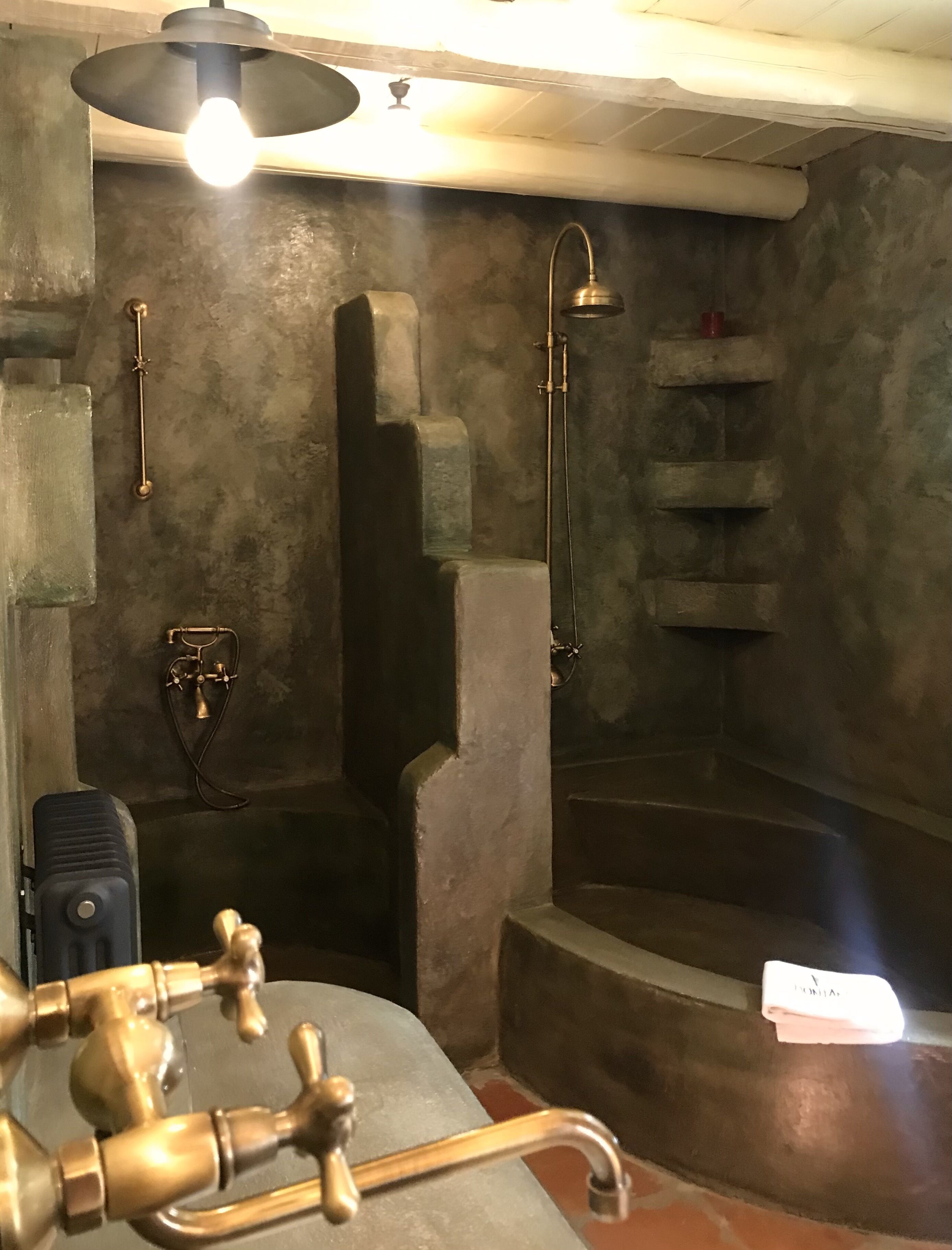 A bathroom with a stone wall, a bathtub, and a shower with a handheld showerhead.